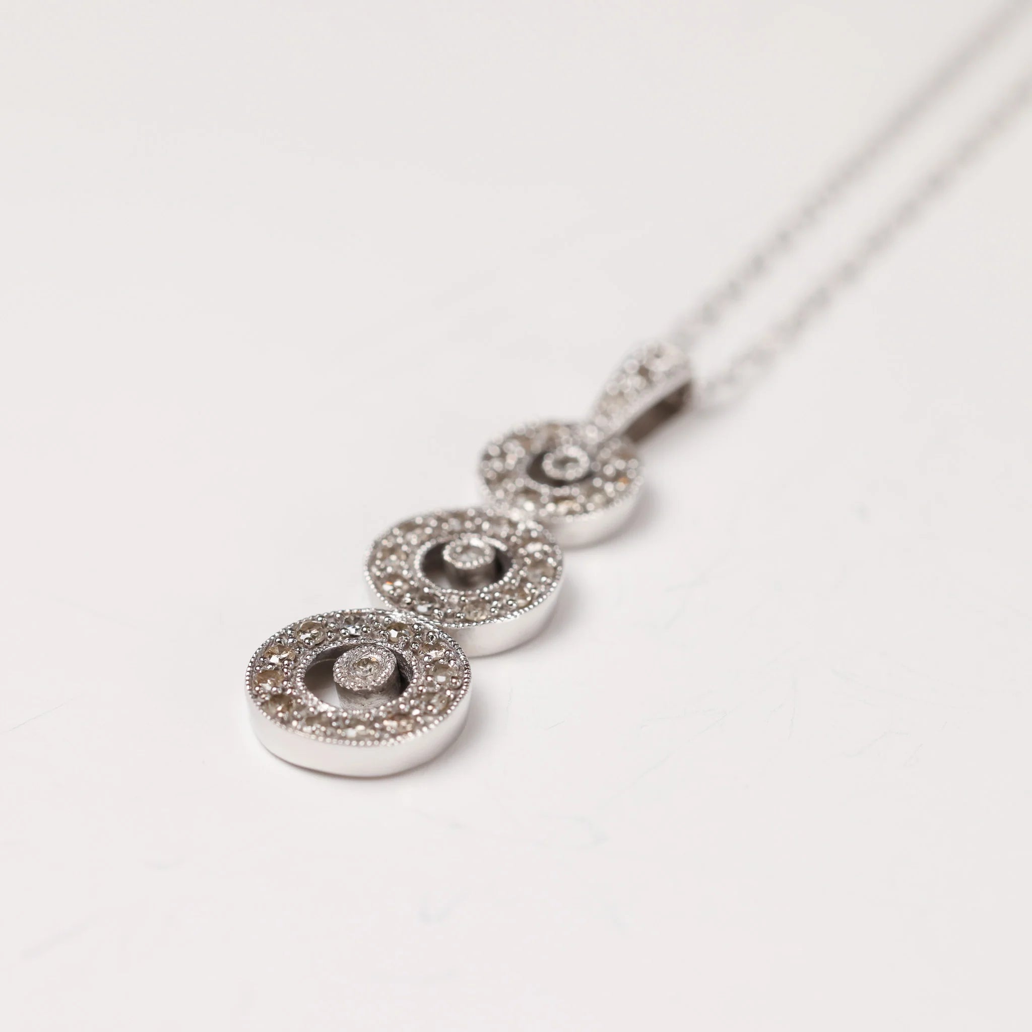 A white gold necklace with a white gold and diamond pendant  laying on a white background