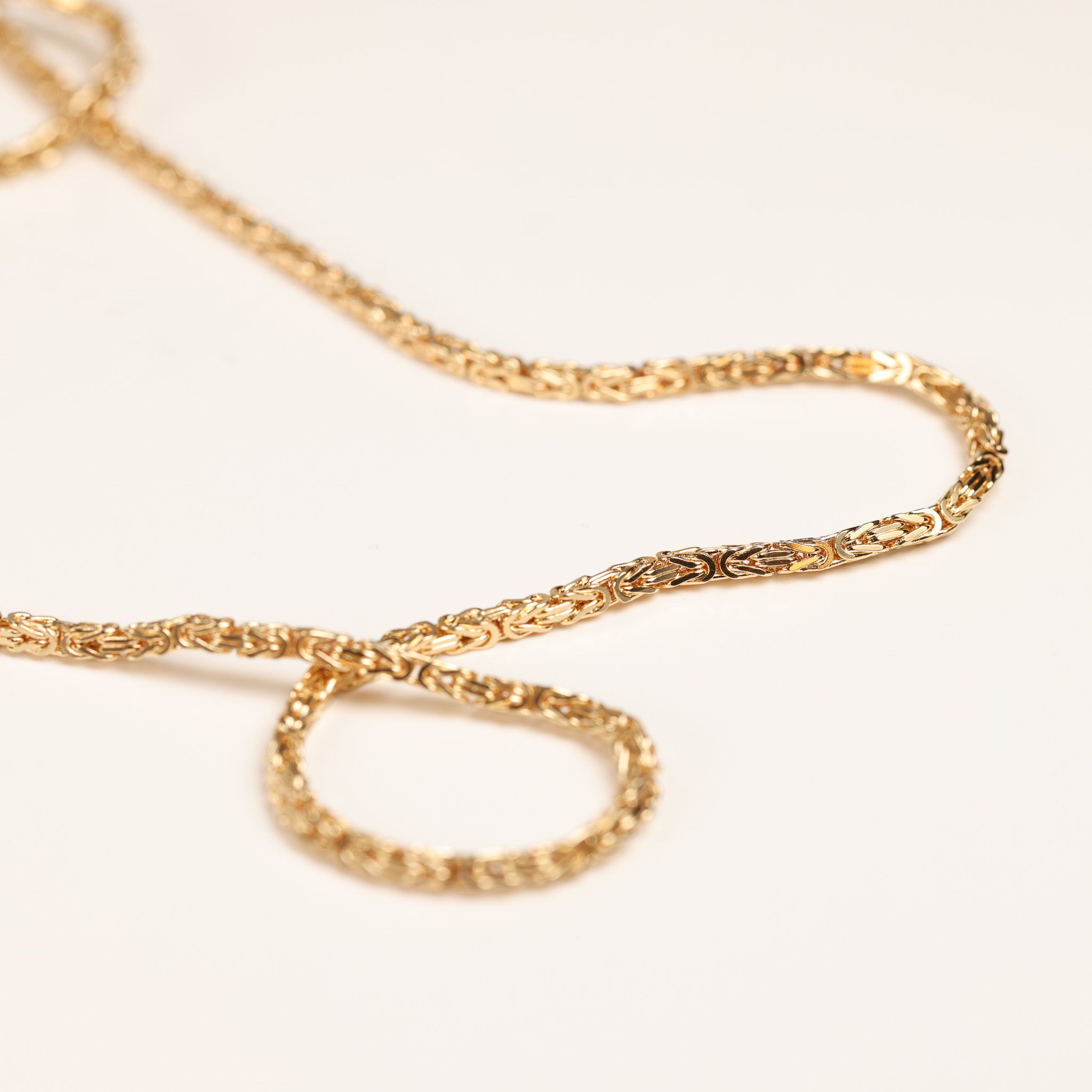 Close-up of a gold chain necklace, intricately woven with a delicate pattern, laid out on a light cream background, alongside a shimmering 14 Karat Yellow Gold Tanzanite Diamond Ring - Size 5.