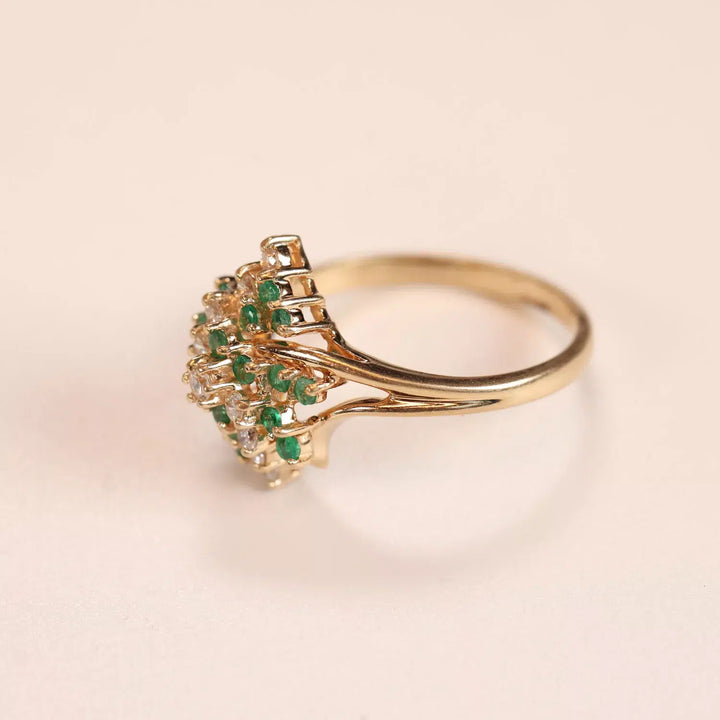 Gold ring with a row of green gemstones on a pale background, accompanied by a 14 Karat Yellow Gold Figaro 25" Chain.