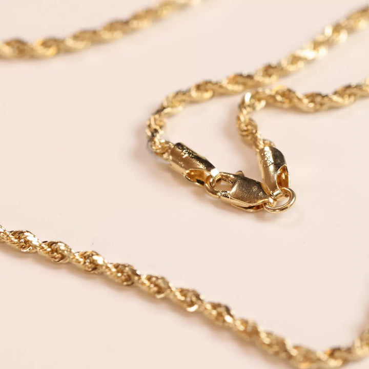 14 Karat Yellow Gold Figaro 25" Chain necklace with a lobster clasp on a pink surface