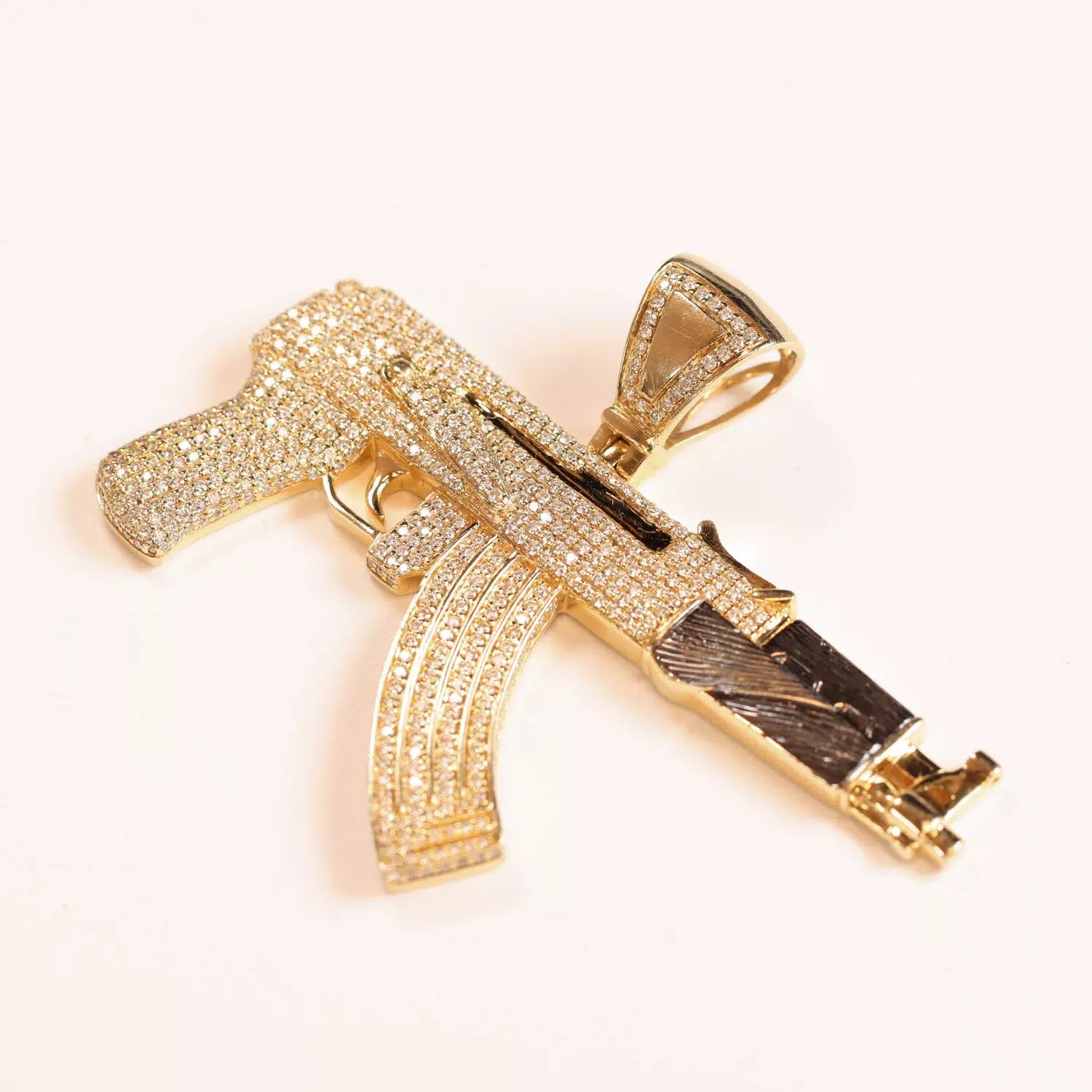 A golden pendant shaped like a gun, embellished with sparkling crystals, hangs from a 14 Karat Yellow Gold Figaro 25" Chain.