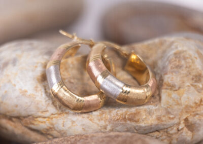 A pair of 14 Karat Yellow Gold White Stone Tennis Bracelet hoop earrings on a rock with a touch of 14 Karat Yellow Gold.