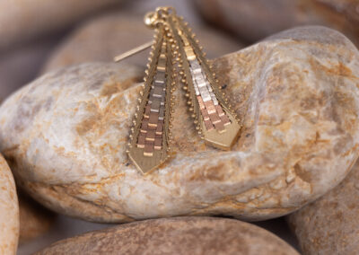 A pair of gold plated earrings laying on top of rocks, surrounded by a 14 Karat Yellow Gold White Stone Tennis Bracelet.