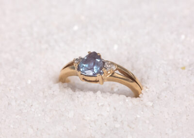 A 14 Karat Yellow Gold Tanzanite & Clear Stone Ring in the sand.