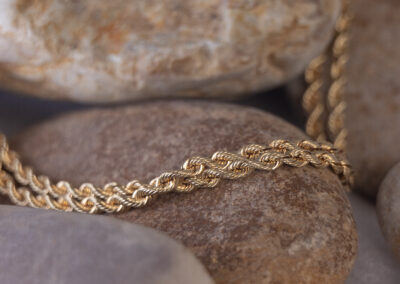 The 14 Karat Yellow Gold Rope Chain is laying on a rock.