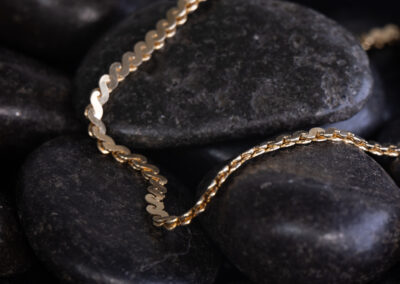 A 14 Karat Yellow Gold White Stone Tennis Bracelet is laying on top of rocks.