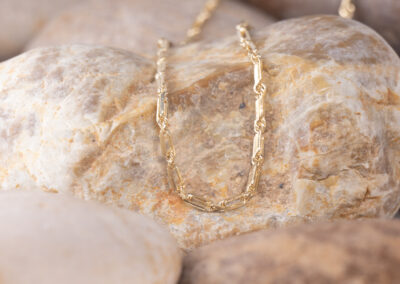 A 14 Karat Yellow Gold White Stone Tennis Bracelet is laying on top of some rocks.