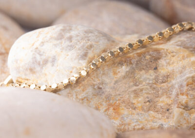 A 14 Karat Yellow Gold Cylindric Bracelet gracefully resting on a bed of rocks.