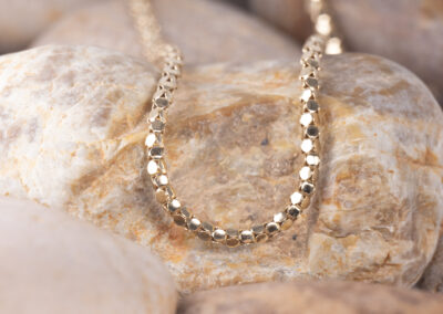 A gold chain necklace is laying on top of rocks, featuring a 14 Karat Yellow Gold White Stone Tennis Bracelet.