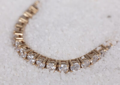 A 14 Karat Yellow Gold White Stone Tennis Bracelet with diamonds laying on top of sand.