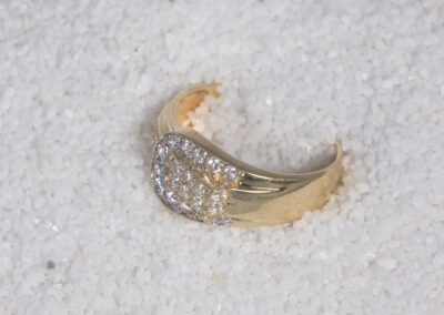 A 14 Karat Yellow Gold White Stone Tennis Bracelet with diamonds sitting on top of sand.