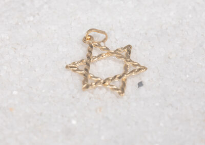 A gold Star of David charm on sand, beautifully complemented by a 14 Karat Yellow Gold White Stone Tennis Bracelet.