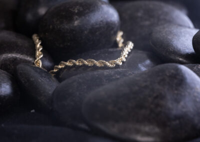 A 14 Karat Yellow Gold White Stone Tennis Bracelet is laying on top of black rocks.