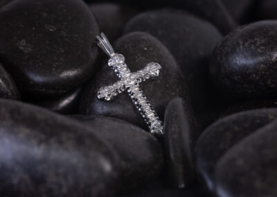 A silver cross on a black background, surrounded by a 14 Karat Yellow Gold White Stone Tennis Bracelet.