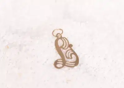 A 14 Karat Yellow Gold Fashion Chain initial charm sitting on top of sand.