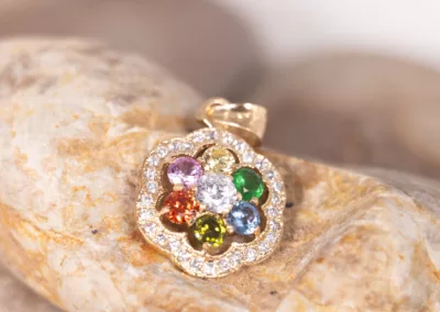A multi colored flower pendant on a rock adorned with a 14 Karat Yellow Gold Fashion Chain.