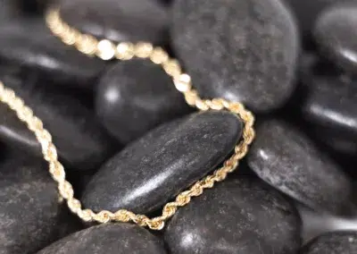 A 14 Karat Yellow Gold Fashion Chain is laying on top of black pebbles.