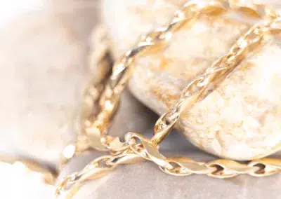 A 14 Karat Yellow Gold Fashion Chain is laying on top of some rocks.