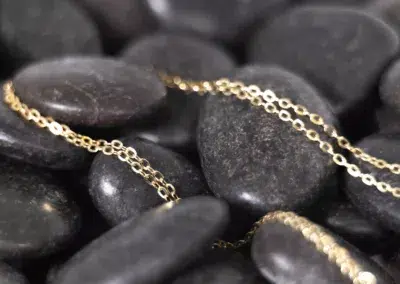 A 14 Karat Yellow Gold Fashion Chain is laying on a pile of rocks.