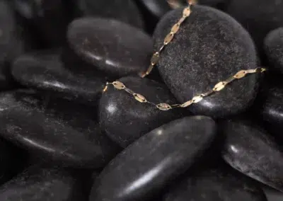 A 14 Karat Yellow Gold Fashion Chain is laying on top of black pebbles.