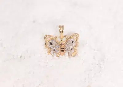 A 14 Karat Yellow Gold Fashion Chain butterfly pendant sitting on top of sand.