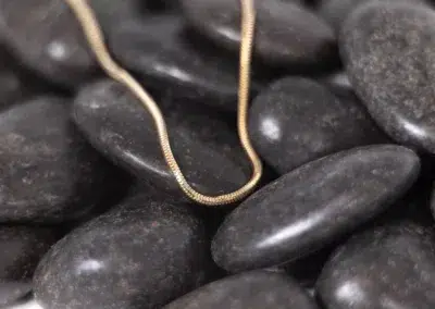 A 14 Karat Yellow Gold Fashion Chain, gracefully laying on a pile of black pebbles.