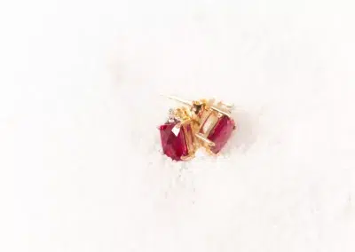 A pair of 14 Karat Yellow Gold Fashion Chain ruby stud earrings sitting on top of snow.