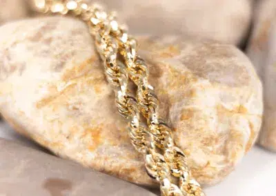 A 14 Karat Yellow Gold Fashion Chain gently resting on top of rocks.