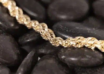 A 14 Karat Yellow Gold Fashion Chain, delicately laid on top of rocks.