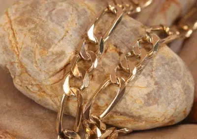 14 Karat Yellow Gold Figaro 25" Chain draped over a stone surface.