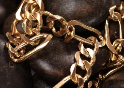 14 Karat Yellow Gold Figaro 25" Chain draped over smooth stones.