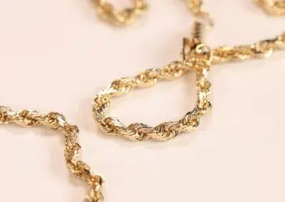 14 Karat Yellow Gold Figaro 25" Chain necklace on a pale pink surface.
