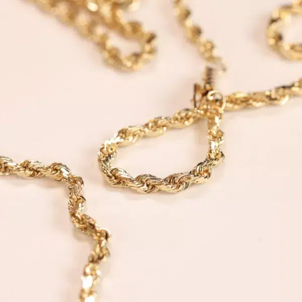 14 Karat Yellow Gold Figaro 25" Chain necklace on a pale pink surface.