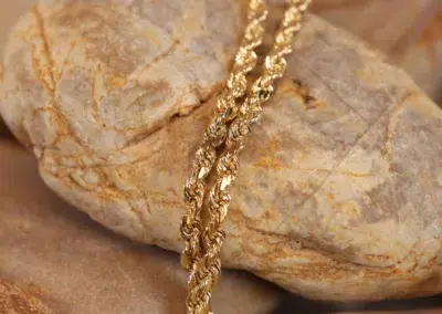 14 Karat Yellow Gold Figaro 25" Chain resting on smooth stones.