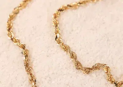 A close-up of a twisted 14 Karat Yellow Gold Figaro 25" Chain on a textured surface.