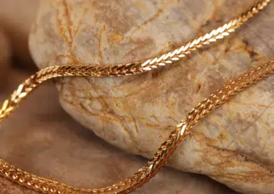 Close-up of a twisted 14 Karat Yellow Gold Figaro 25" Chain resting on a textured stone surface.