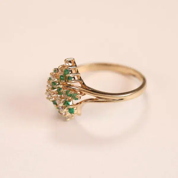 Gold ring with a row of green gemstones on a pale background, accompanied by a 14 Karat Yellow Gold Figaro 25" Chain.