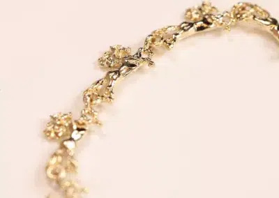 Close-up of a 14 Karat Yellow Gold Figaro 25" Chain with floral design elements on a pink background.