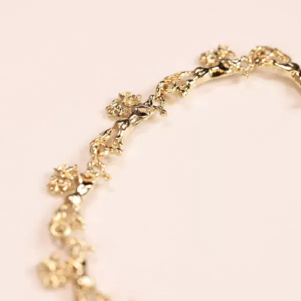 Close-up of a 14 Karat Yellow Gold Figaro 25" Chain with floral design elements on a pink background.