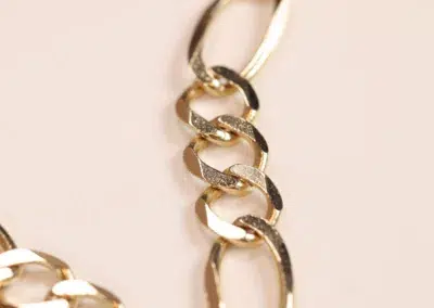 Close-up of a 14 Karat Yellow Gold Figaro 25" chain with interlocking links on a pastel background.