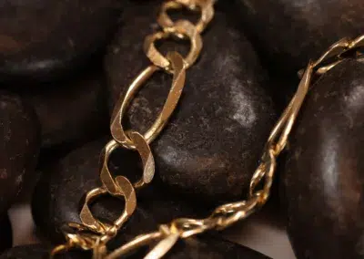 A 14 Karat Yellow Gold Figaro 25" Chain draped over smooth dark stones.