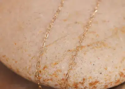 14 Karat Yellow Gold Figaro 25" chain necklace on a textured stone surface.