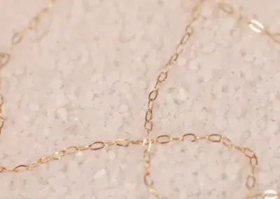 A delicate 14 Karat Yellow Gold Figaro 25" Chain necklace on a bed of fine, white granular substance.