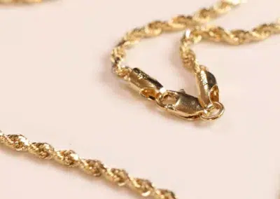 14 Karat Yellow Gold Figaro 25" Chain necklace with a lobster clasp on a pink surface