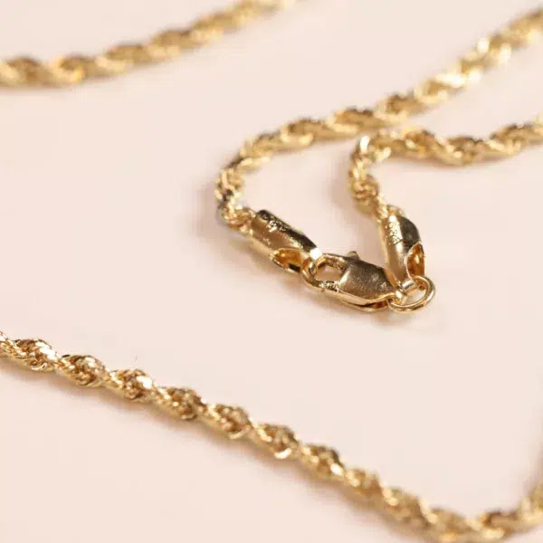 14 Karat Yellow Gold Figaro 25" Chain necklace with a lobster clasp on a pink surface
