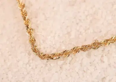 A 14 Karat Yellow Gold Figaro 25" chain necklace on a textured beige background.