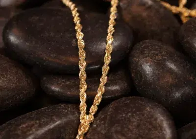 14 Karat Yellow Gold Figaro 25" Chain draped over smooth dark stones.