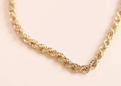 14 Karat Yellow Gold Figaro 25" Chain necklace on a light pink background.