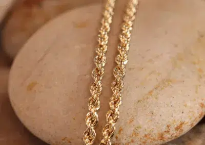 14 Karat Yellow Gold Figaro 25" Chain resting on a smooth stone surface.