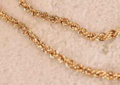 Close-up of two intertwined 14 Karat Yellow Gold Figaro 25" chains on a textured surface.